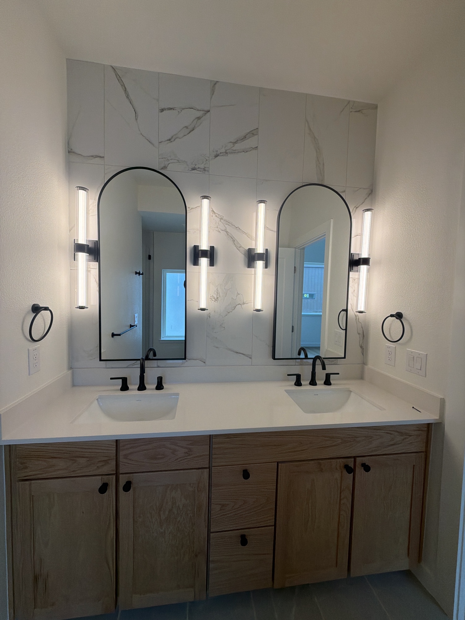 Double vanity with arched mirrors and marble tile wall — Roaring Lion Renovation
