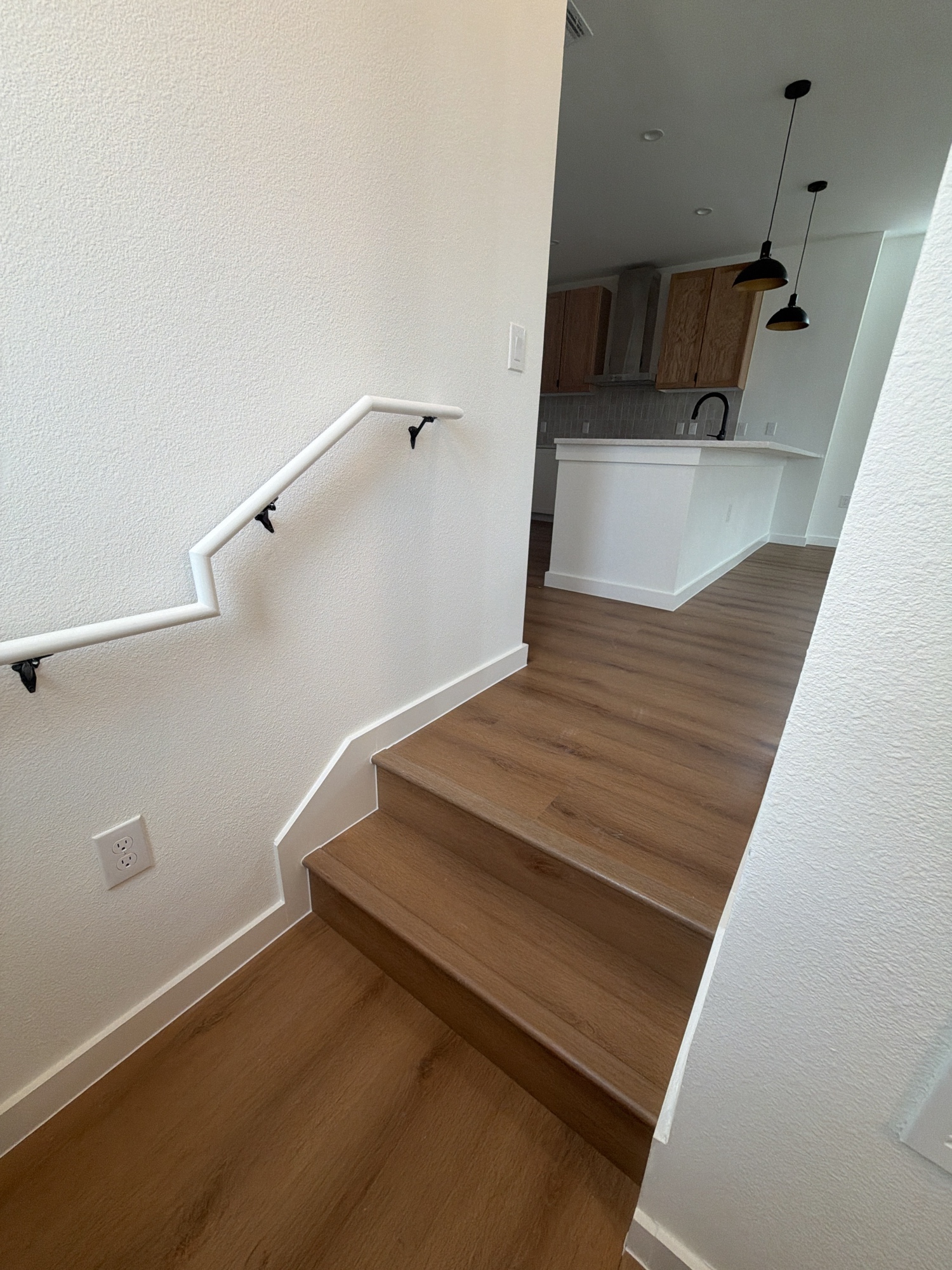 Finished staircase overlooking kitchen with LVP flooring and pendant lights